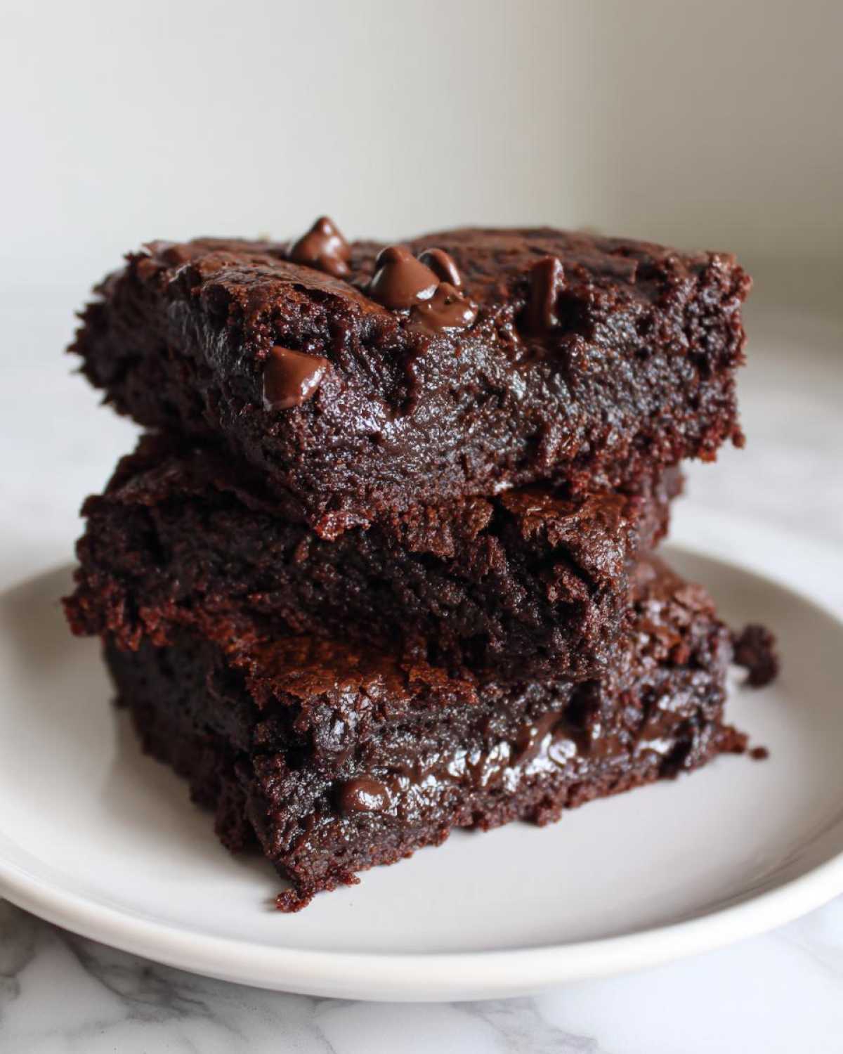 A stack of two rich, fudgy sweet potato brownies topped with melted chocolate chips on a white plate.