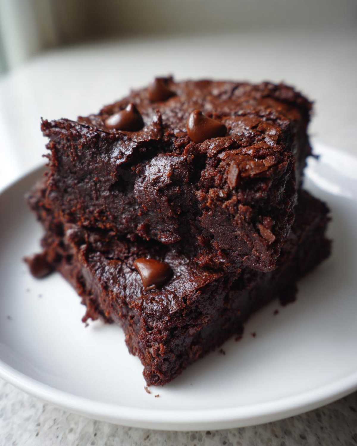 Two fudgy sweet potato brownies stacked on a white plate, topped with melted chocolate chips.