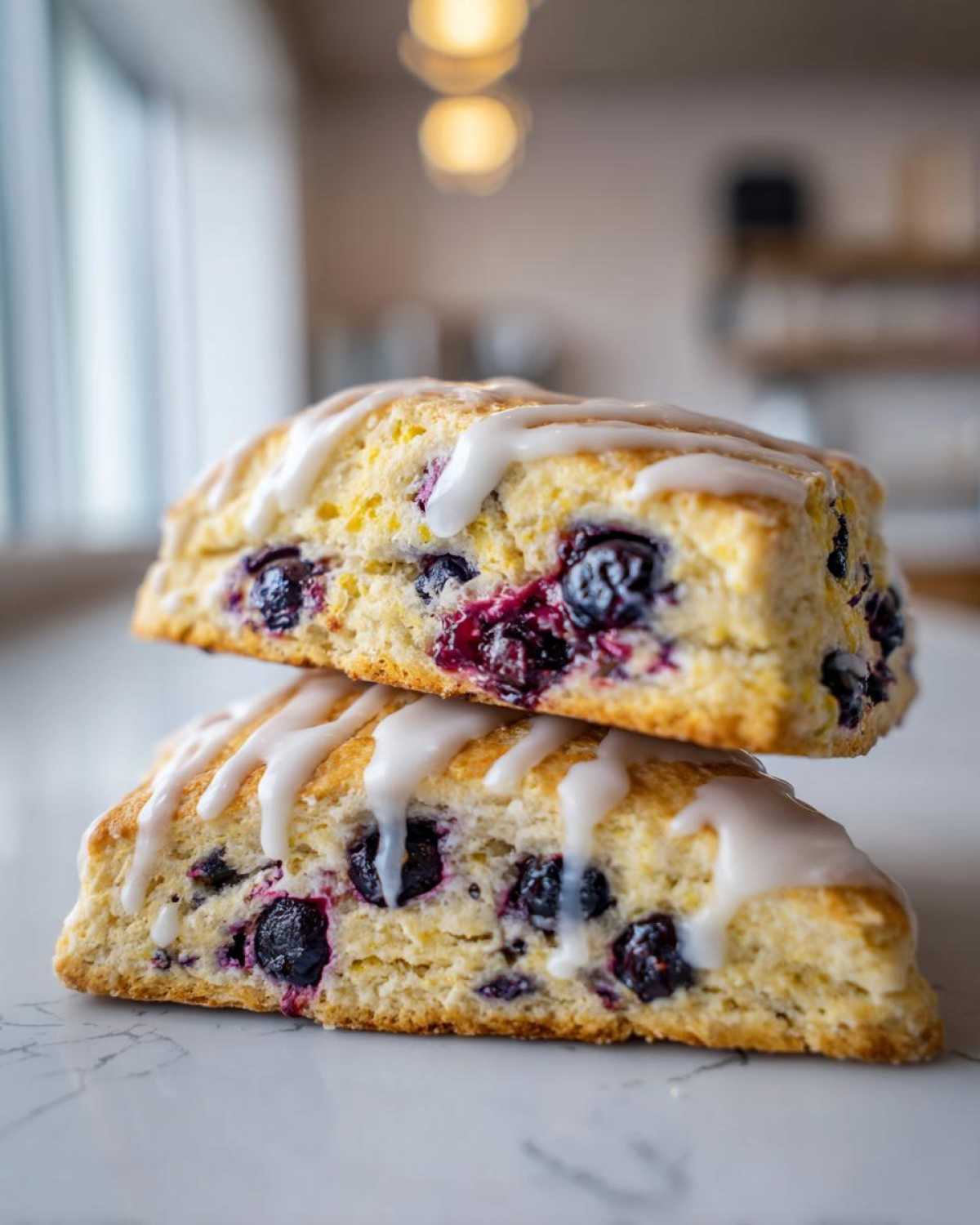 Two triangular blueberry scones stacked, drizzled generously with white lemon glaze.