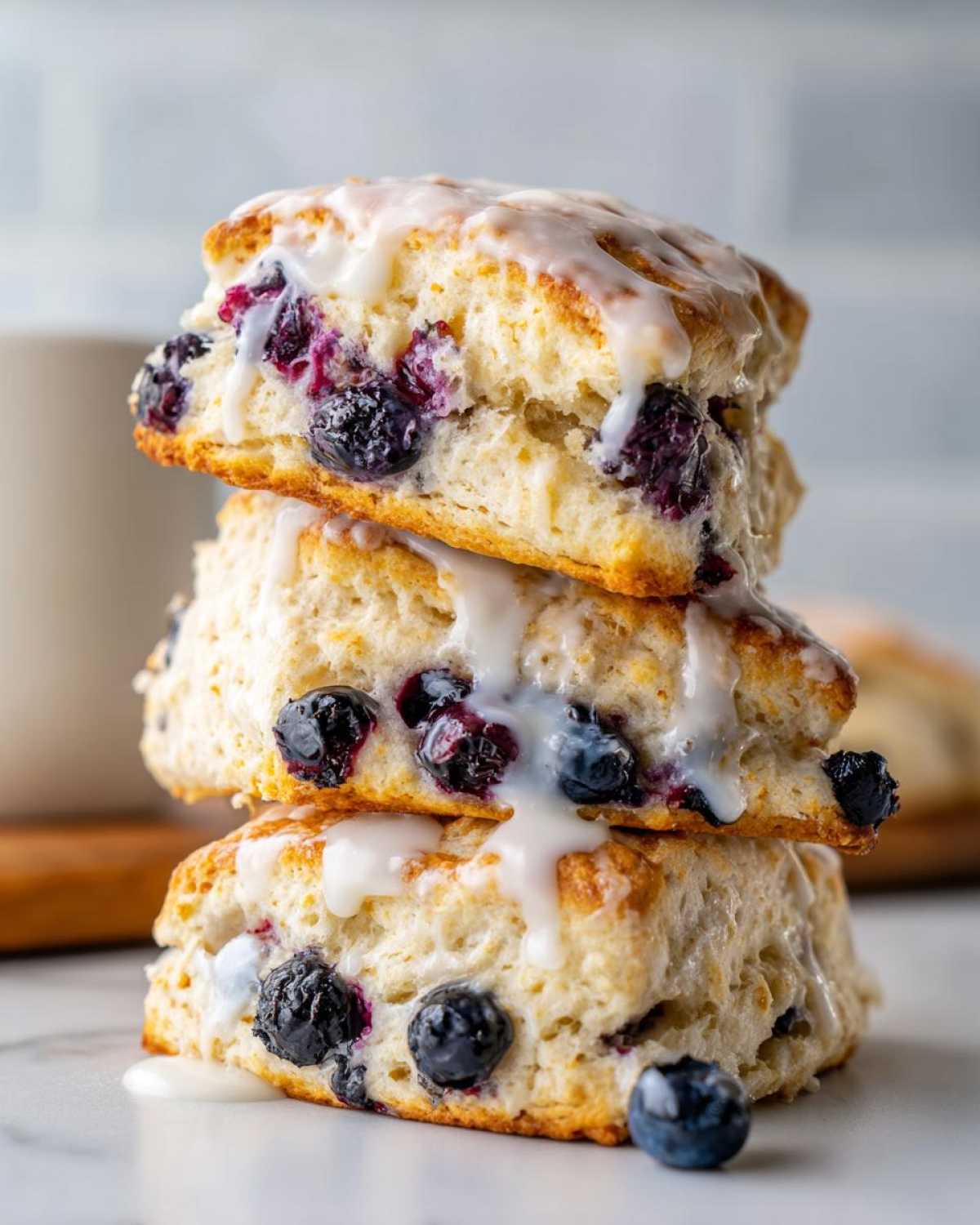 Three stacked, freshly baked blueberry scones drizzled with white lemon glaze.