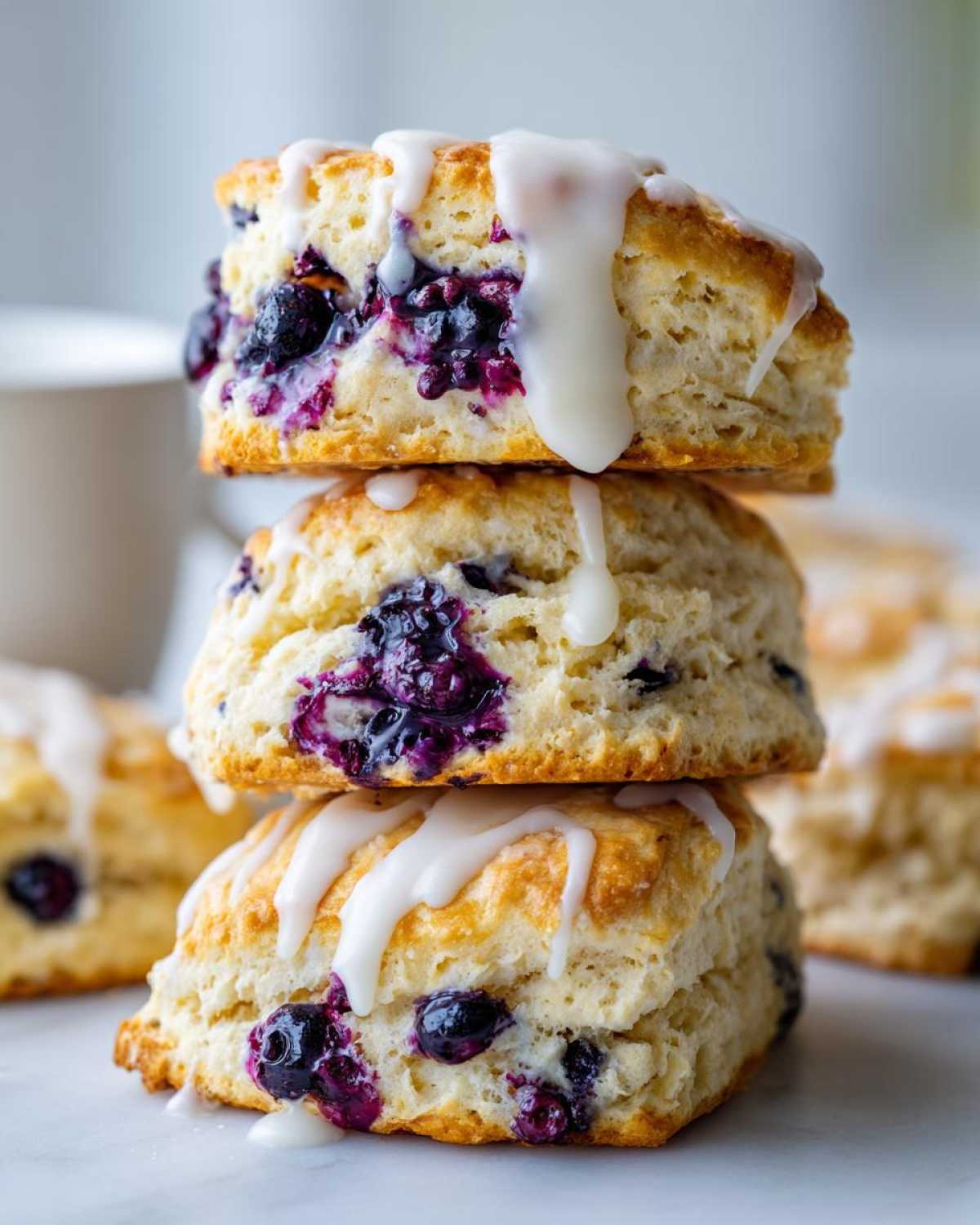 Three glazed blueberry scones stacked vertically, featuring visible blueberries and white lemon glaze.