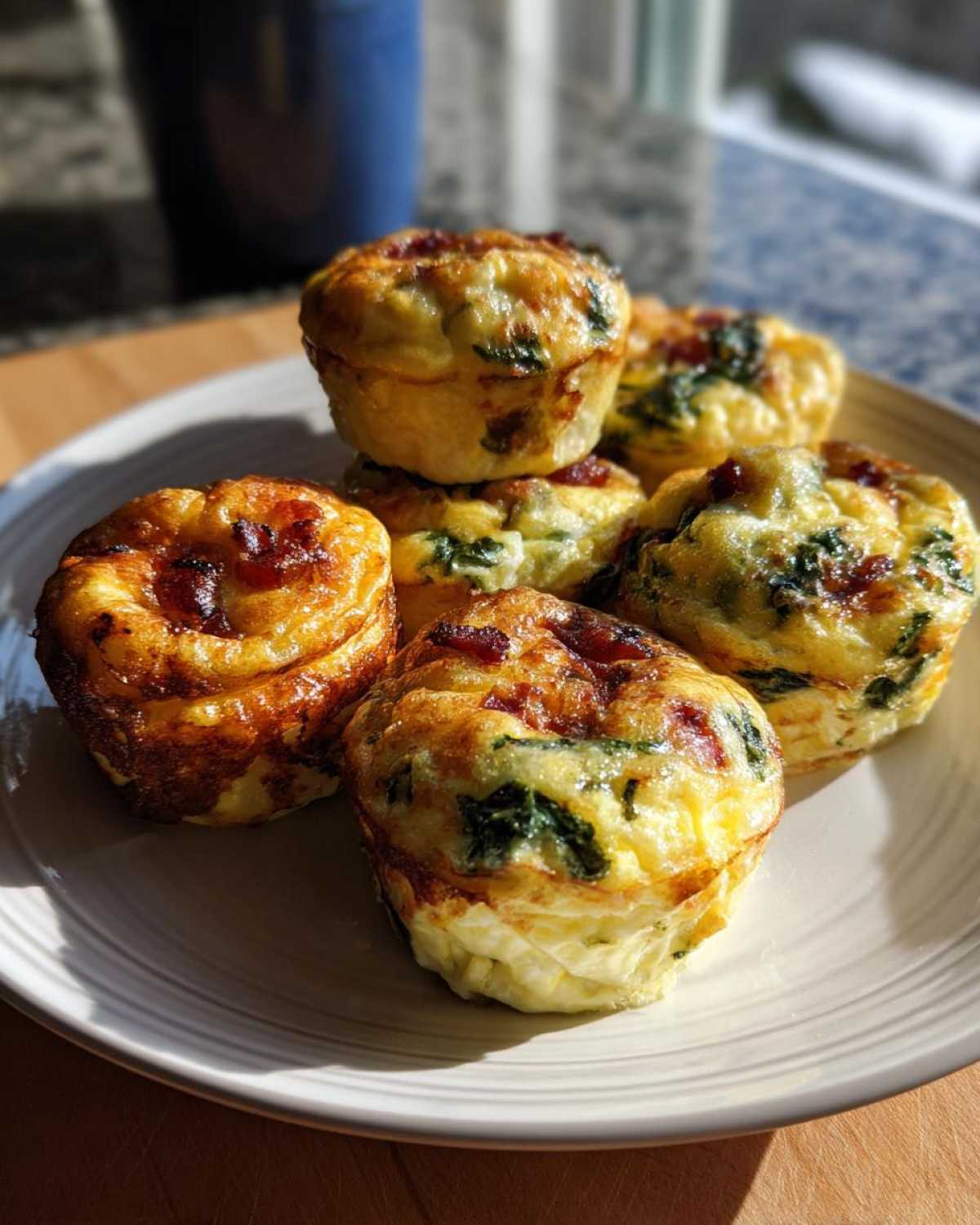 A stack of freshly baked, golden brown egg bites containing visible spinach and meat, resting on a light plate.