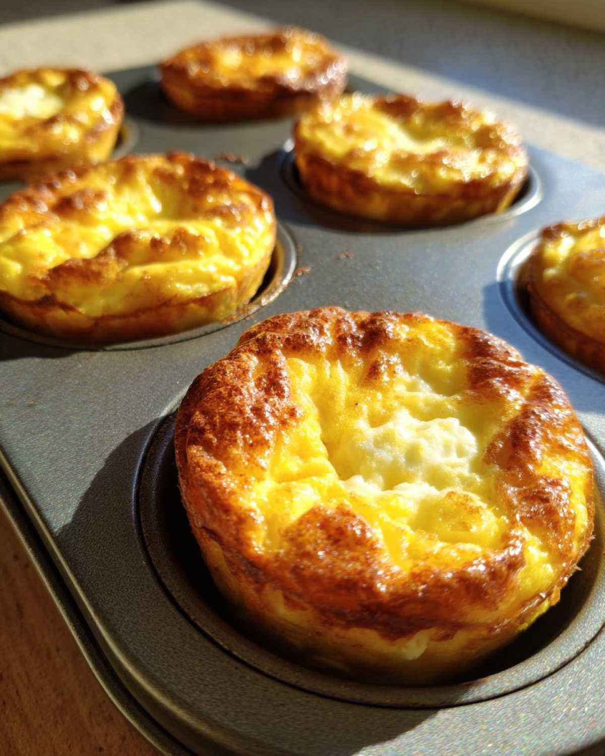 Close-up of golden-brown baked Egg Muffin Cups still sitting in a dark metal muffin tin.