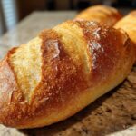 Close-up of a perfectly baked, golden brown French bread loaf with a crisp, scored crust sitting on a granite countertop.