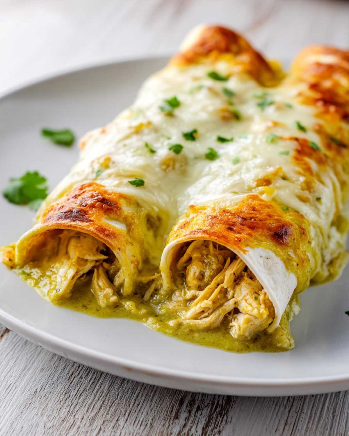 Close-up of two green chile chicken enchiladas smothered in melted, slightly browned cheese and cilantro.