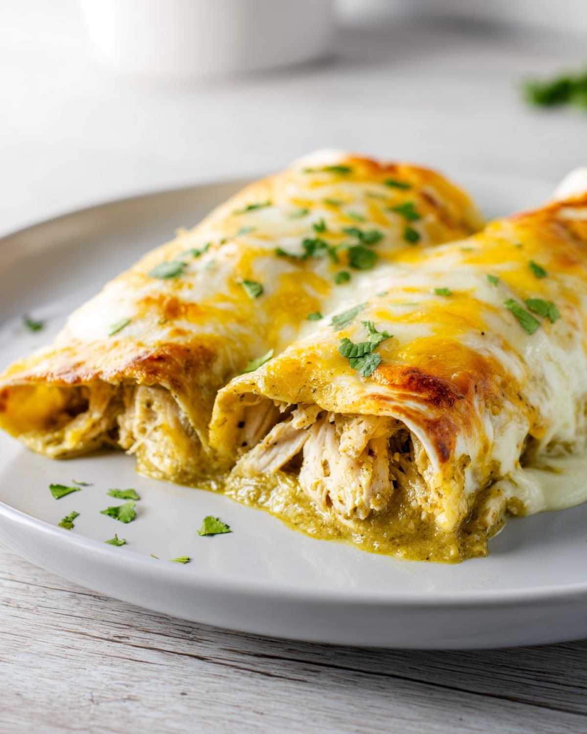 Two green chile chicken enchiladas covered in melted white and yellow cheese and garnished with cilantro.