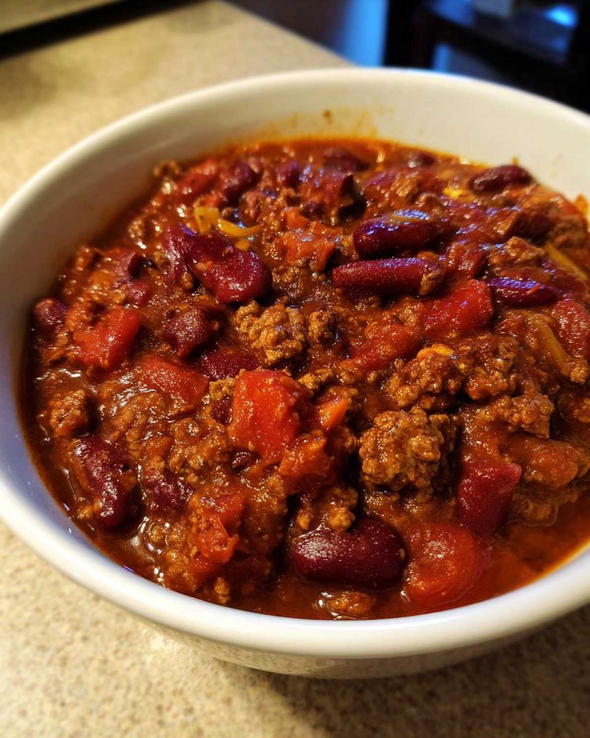 Close-up of a white bowl filled with rich, thick crockpot chili featuring ground beef, kidney beans, and diced tomatoes.