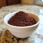 A close-up of rich, dark brown homemade hot cocoa mix powder mounded in a small white bowl.