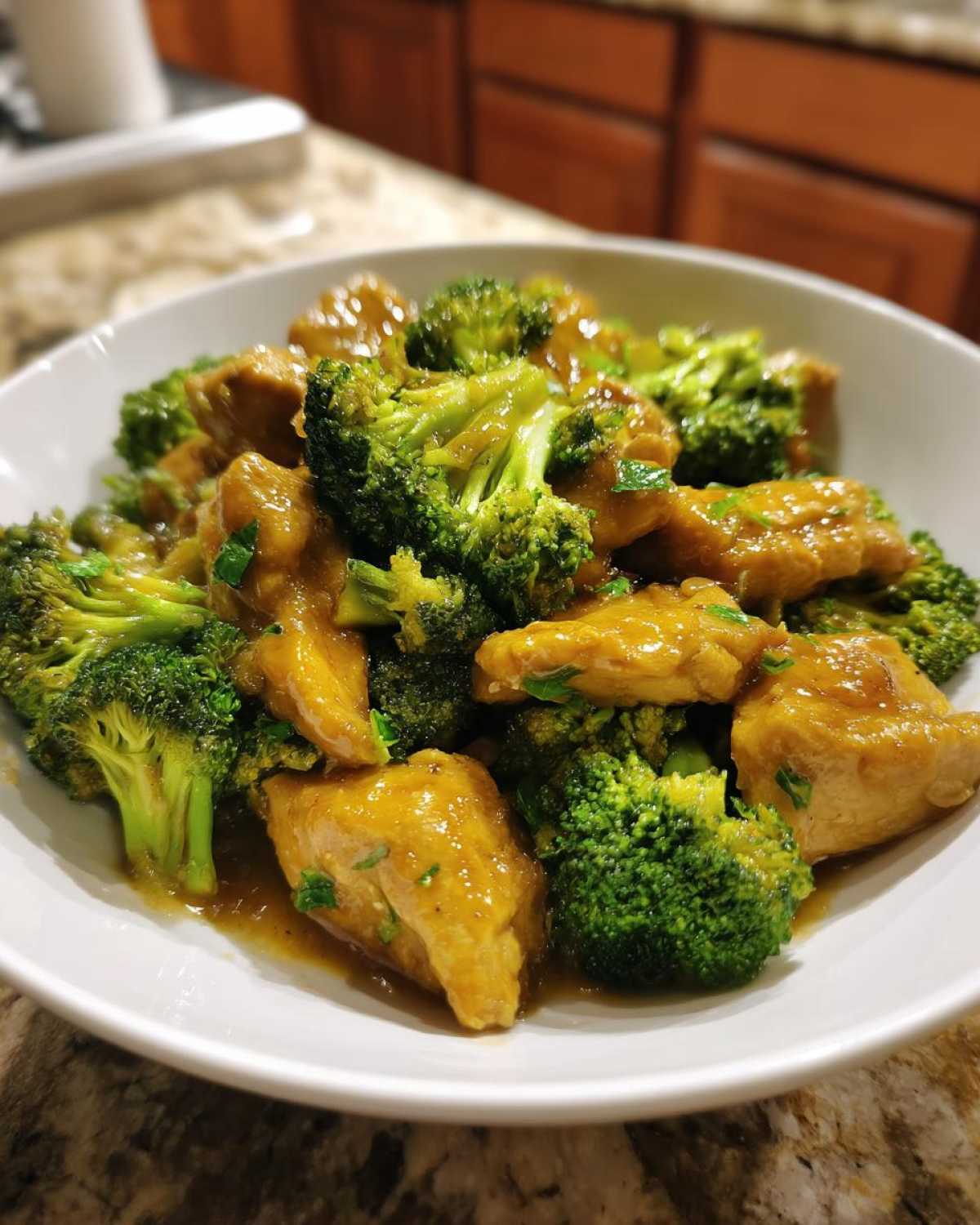 Close-up of tender chicken pieces and bright green broccoli florets coated in honey garlic sauce.