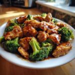 Close-up of glistening honey garlic chicken and broccoli served on a white plate.