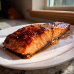 A perfectly cooked fillet of honey garlic salmon glazed with a dark, sticky sauce, resting on a white plate.
