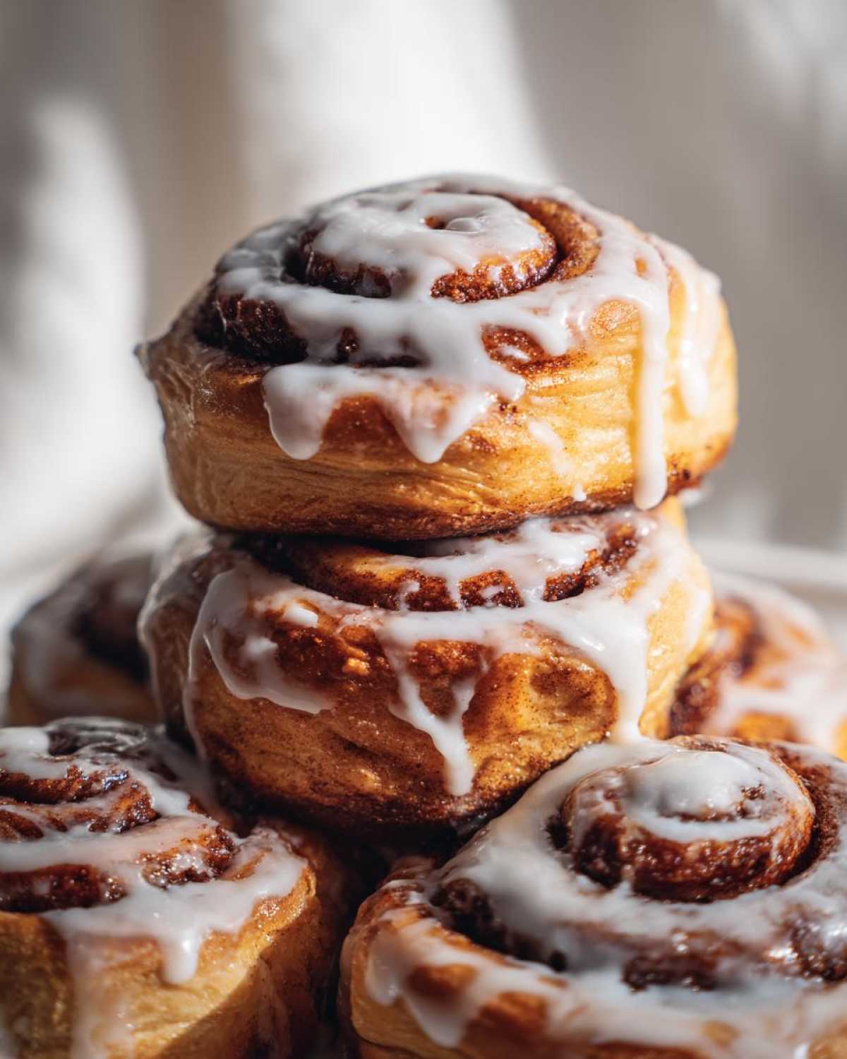 A close-up stack of freshly baked cinnamon rolls generously drizzled with white icing.