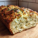 A golden-brown loaf of Italian herb and cheese bread, sliced open to show the soft interior and melted cheese.