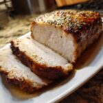 Close-up of a perfectly cooked pork loin roast, sliced to show juicy interior and herb crust.