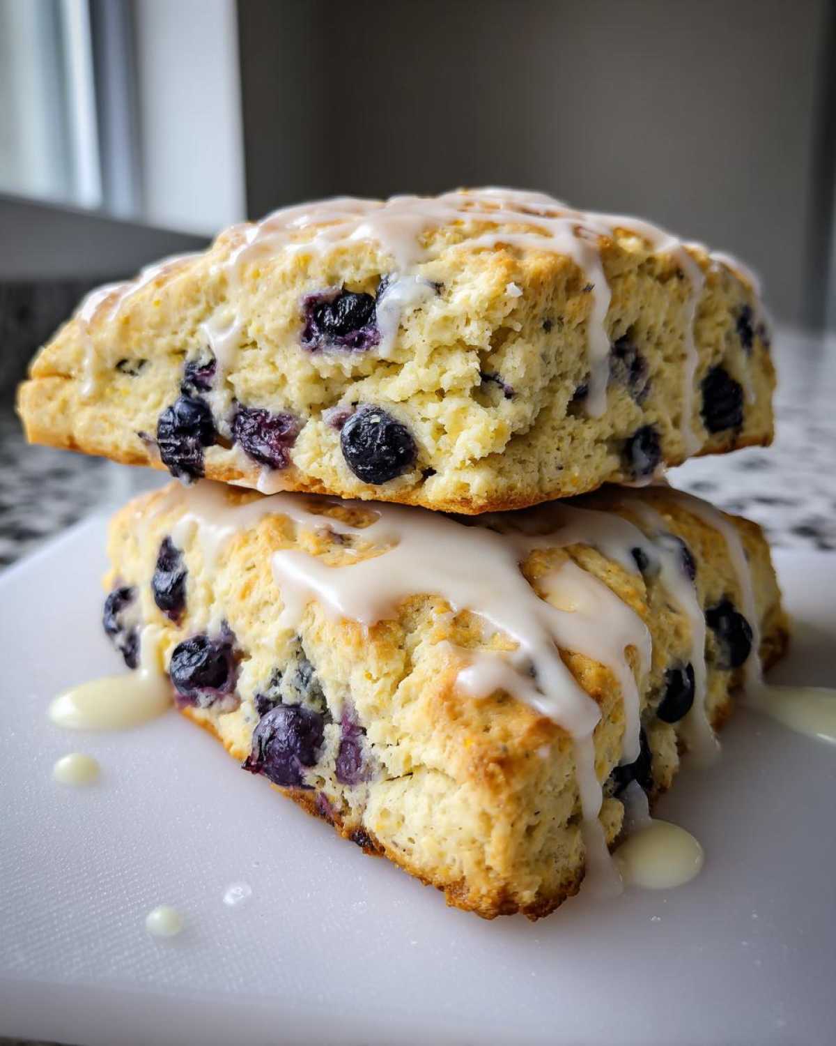 Two stacked, freshly baked blueberry scones drizzled generously with a thick lemon glaze.