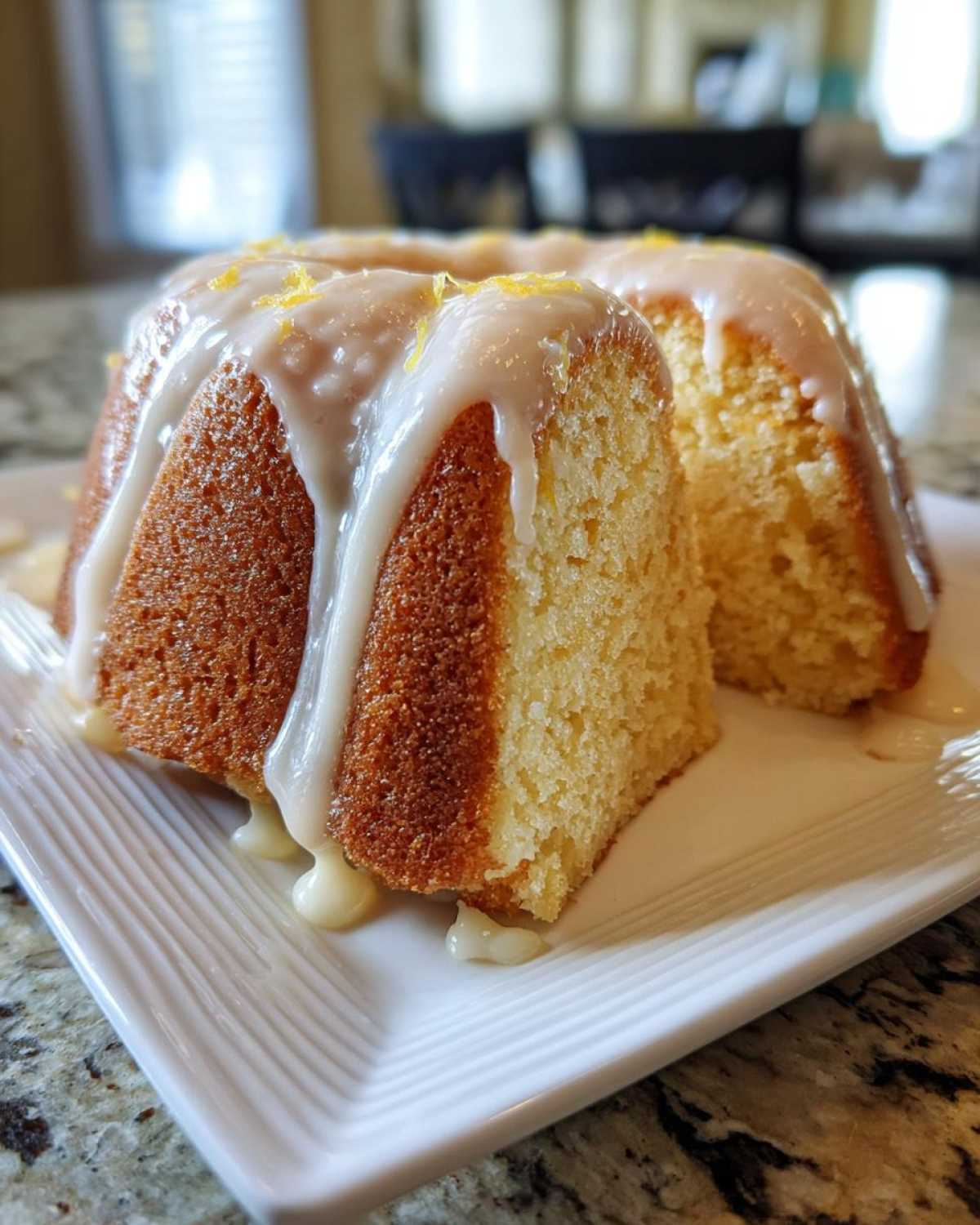 A close-up of a slice cut from a lemon pound cake, topped with thick white glaze and lemon zest.