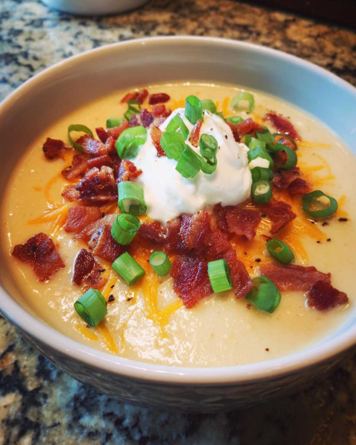 A creamy bowl of loaded baked potato soup topped generously with bacon bits, shredded cheese, sour cream, and green onions.