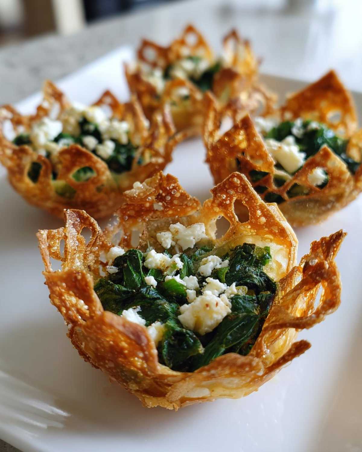 Close-up of crispy baked wonton cups filled with sautéed spinach and crumbled feta cheese, showcasing Mediterranean Spinach and Feta Cheese Crisps.