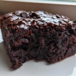 Close-up of a rich, dark slice of black bean brownies topped with melted chocolate chips on a white plate.