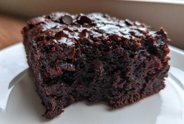Close-up of a rich, dark slice of black bean brownies topped with melted chocolate chips on a white plate.
