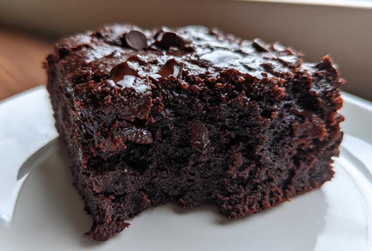 Close-up of a rich, dark slice of black bean brownies topped with melted chocolate chips on a white plate.