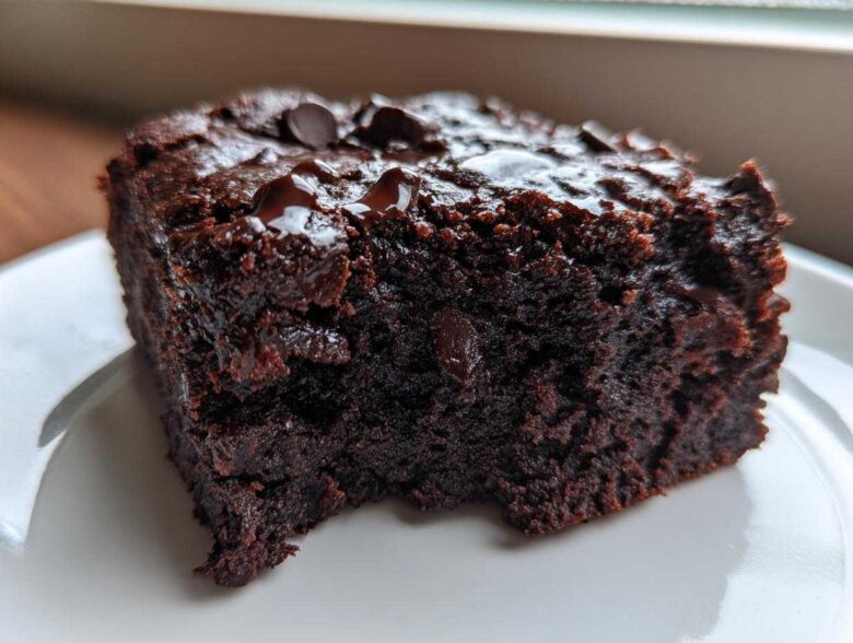 Close-up of a rich, dark slice of black bean brownies topped with melted chocolate chips on a white plate.