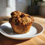 A single, perfectly baked bran muffin topped with raisins resting on a small white plate.