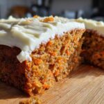 Close-up of a moist slice of carrot cake recipe showing shredded carrots and thick cream cheese frosting.