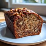 A close-up of a moist slice of date nut bread, featuring visible walnuts throughout the crumb and on top.