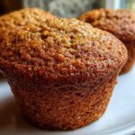 Close-up of a perfectly baked, moist honey bran muffins with a glossy, dark brown top on a white plate.