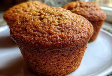 Close-up of a perfectly baked, moist honey bran muffins with a glossy, dark brown top on a white plate.