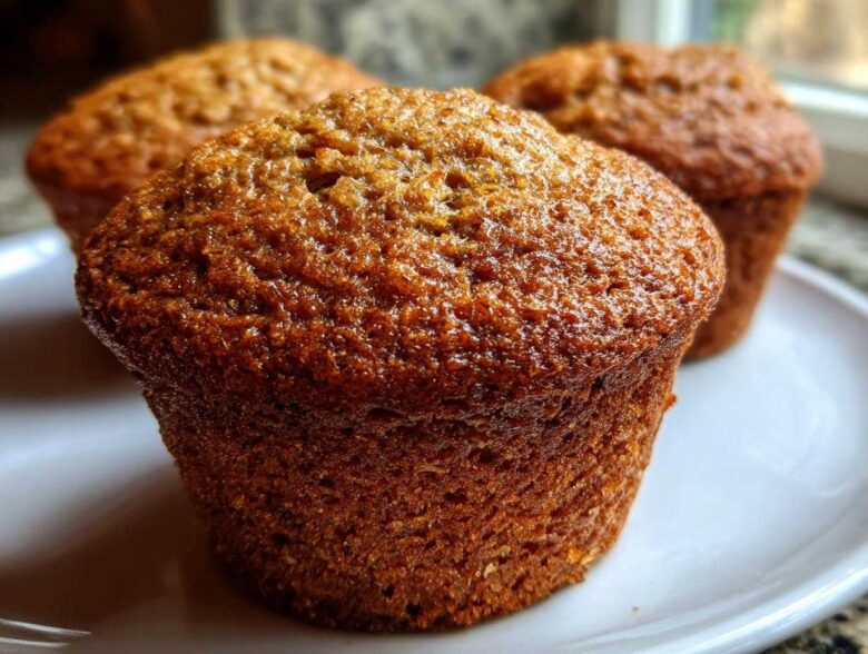 Close-up of a perfectly baked, moist honey bran muffins with a glossy, dark brown top on a white plate.