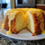 A lemon pound cake, cut in half to show the moist interior, covered in a thick yellow lemon glaze.