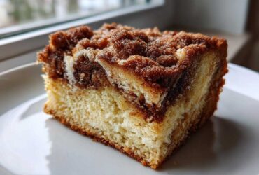 A close-up of a moist slice of sour cream coffee cake featuring a thick cinnamon streusel topping.