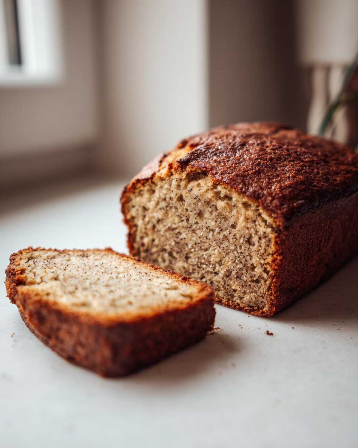 A close-up of a freshly baked loaf of sugar free banana bread with one thick slice cut and resting beside it.
