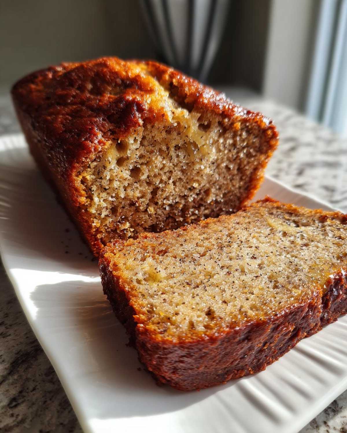 A close-up of a moist slice cut from a loaf of sugar free banana bread, showing the texture and dark crust.