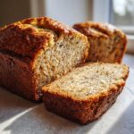 Close-up of moist sugar free banana bread loaf with one thick slice cut and resting beside it.