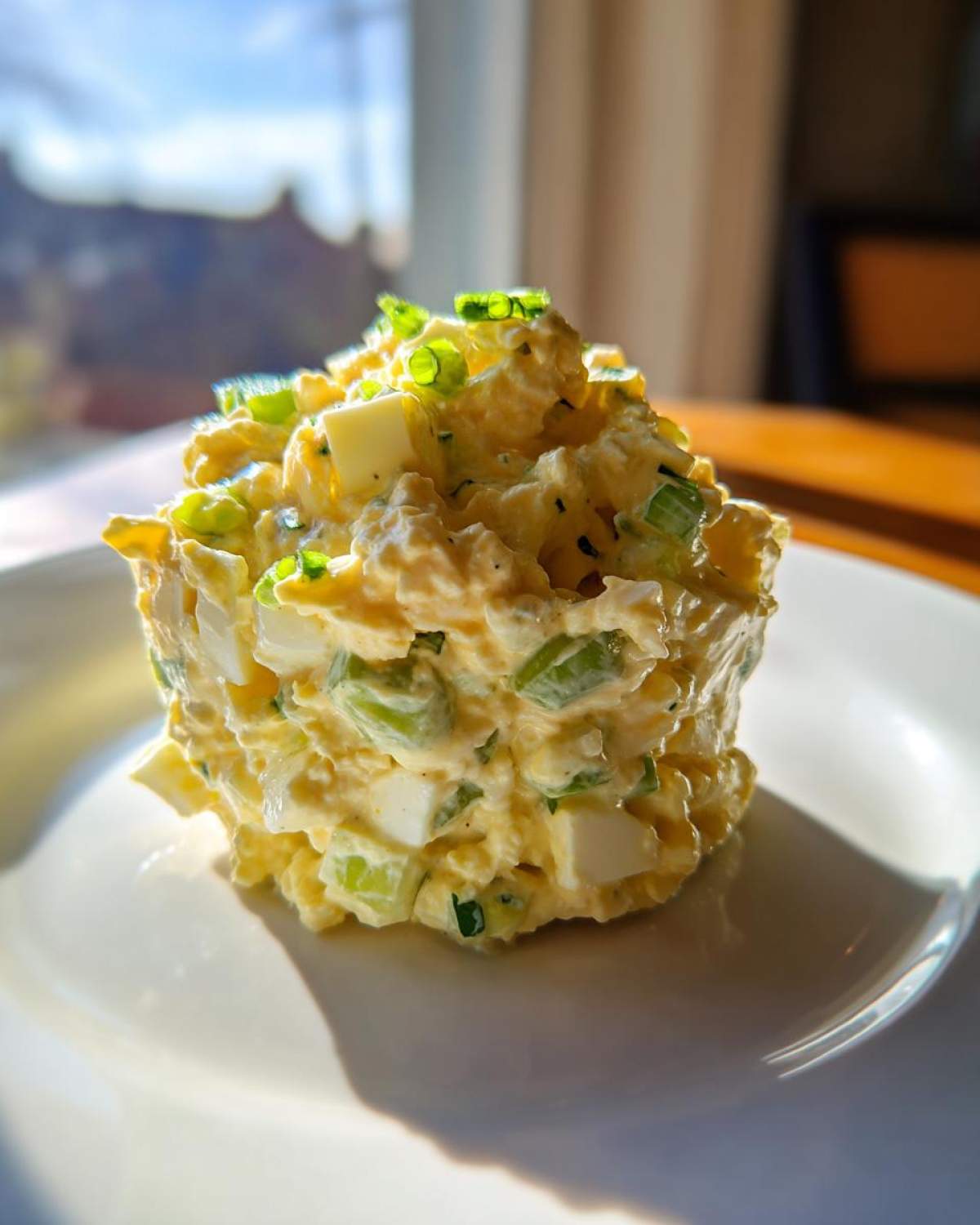 A beautifully molded portion of creamy egg salad recipe, topped with fresh green onions, served on a white plate.