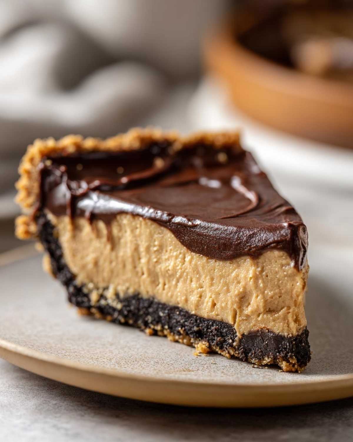 A close-up slice of no-bake peanut butter pie featuring a dark crust, creamy filling, and rich chocolate ganache topping.