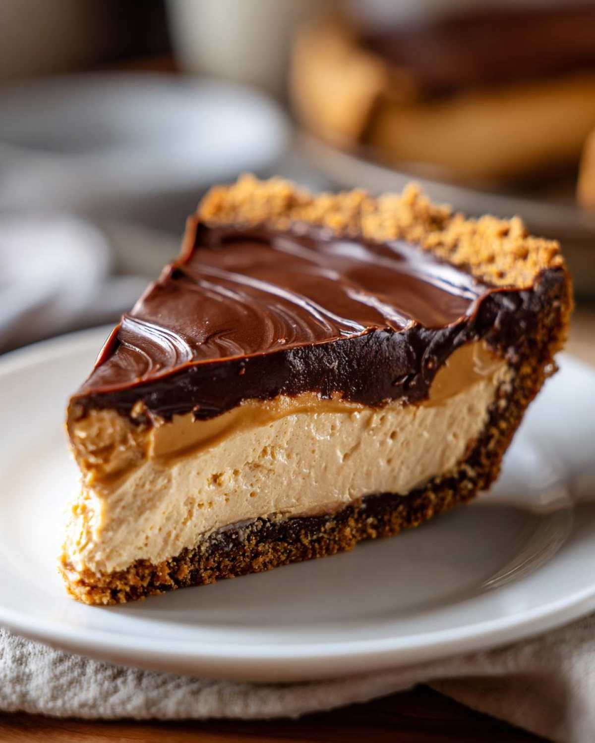 A decadent slice of no-bake peanut butter pie featuring a thick peanut butter filling and rich chocolate ganache topping.