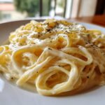 Close-up of fettuccine pasta generously coated in creamy Olive Garden Alfredo sauce and sprinkled with herbs.