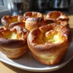Close-up of several golden brown, perfectly risen yorkshire pudding on a white plate.