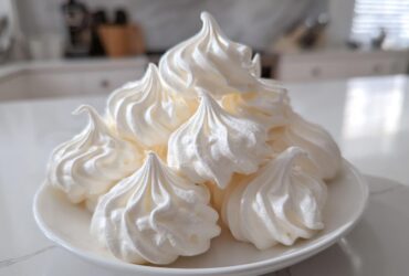A pile of perfectly piped, glossy white meringue cookies stacked on a small white plate.