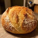 Close-up of a golden-brown, crusty round loaf of homemade french bread dusted with flour.