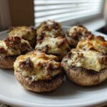 A close-up of several baked sausage stuffed mushrooms topped with melted, browned cheese served on a white plate.