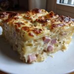 A thick, square slice of creamy scalloped potatoes and ham with a golden, bubbly cheese crust.