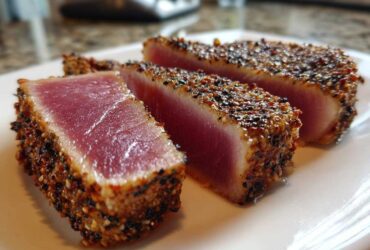 Three thick slices of perfectly Seared Ahi Tuna showing a rare, deep pink center and a dark sesame seed crust.