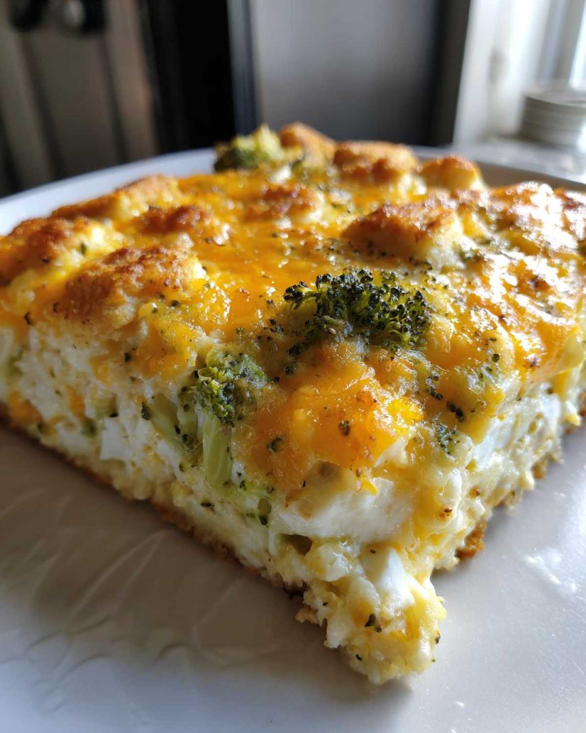 Close-up of a square slice of chicken broccoli rice casserole topped with melted cheddar cheese.