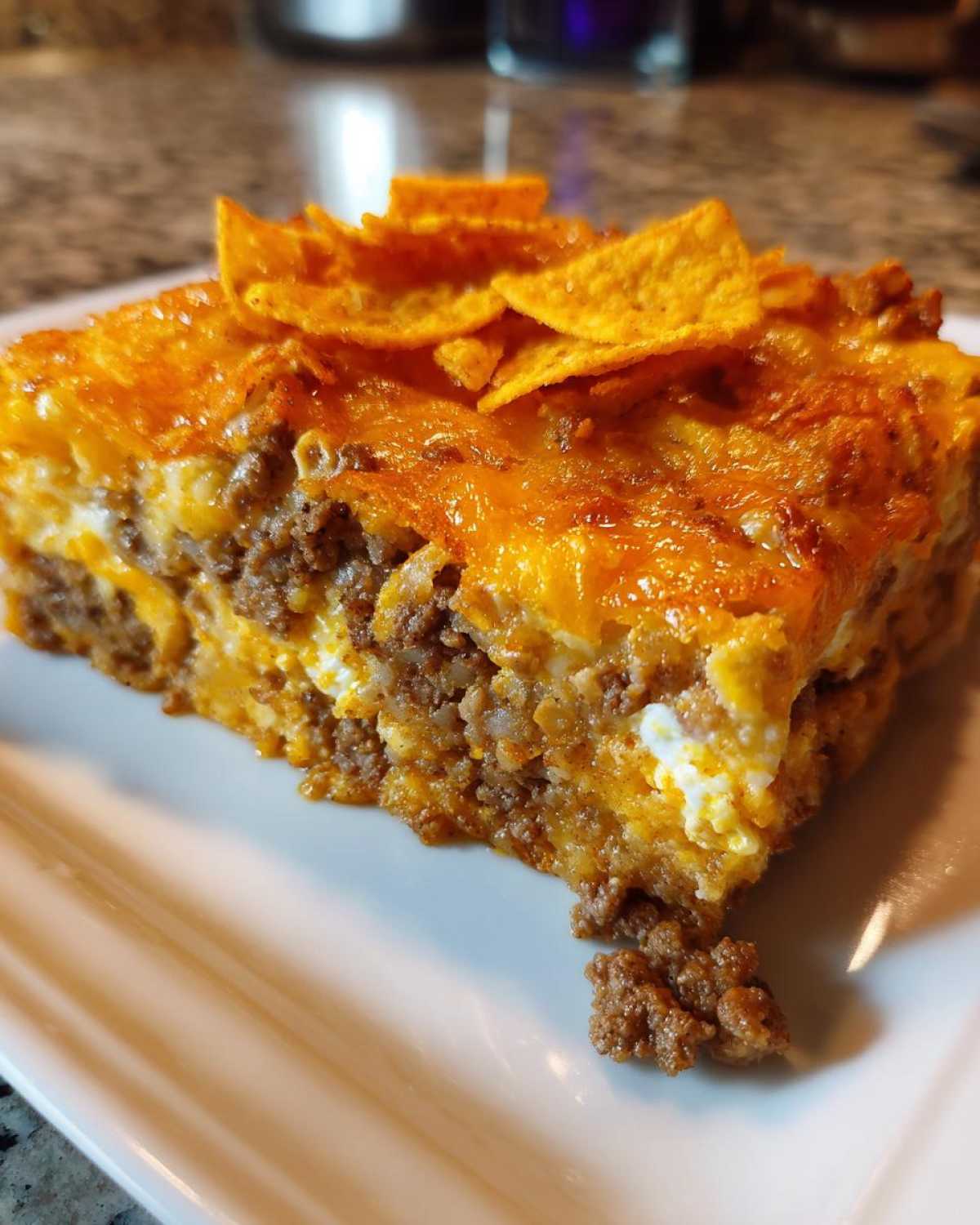 A close-up slice of Dorito Casserole featuring layers of seasoned ground beef, cheese, and topped with whole Doritos.