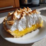A perfect slice of lemon meringue pie showing bright yellow filling and tall, toasted meringue peaks.